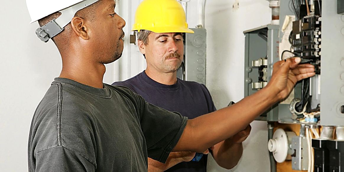Two electricians in hard hats working on an electrical panel