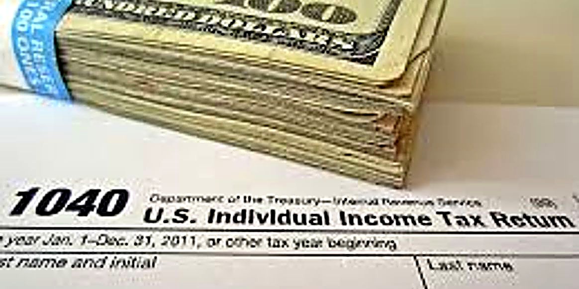 A folded stack of hundred-dollar bills resting on a Form 1040 U.S. Individual Income Tax Return
