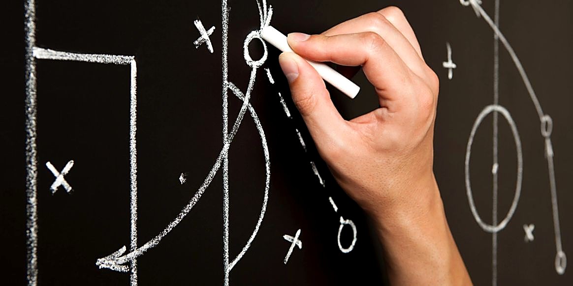 A hand drawing a play diagram in chalk on a blackboard
